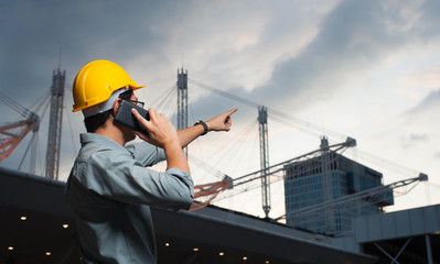 Engineer is pointing the job,Engineer  is setting goal,Engineer is controlling the construction on twilight bacground,Engineer using a mobile phone to contact the job