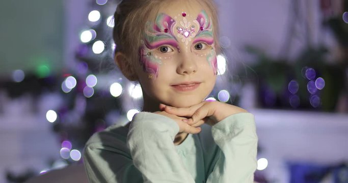 A cute little girl with bright make-up looks at the camera and smiles.