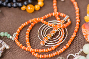Serdolik (carnelian) stone necklace laying on natural brown linen tablecloth. Yashma, orange jasper, onyx gemstones around. Healing, powerful energy for crystal therapy treatments. Esoteric background