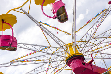 Colorful roller coaster seats at amusement park. People having fun in carousel. Wheel is spinning fast.