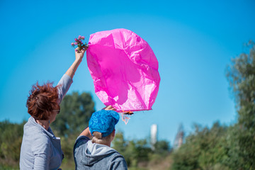 Mom and son celebrating his birthday and preparing a pink fire lantern to let it go with the wind on clear blue sky background