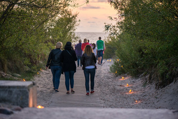 Romantic bonfire night at seaside during sunset. People gathering together to celebrate Night of ancient lights. Walking on wooden pathway on seaside on lit candle path during sunset.