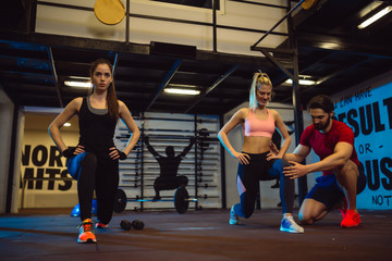 Two young and fit girls are exercising in gym with their personal trainer