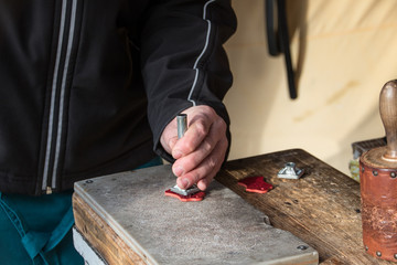 Male using leather stamp on a piece of red leather