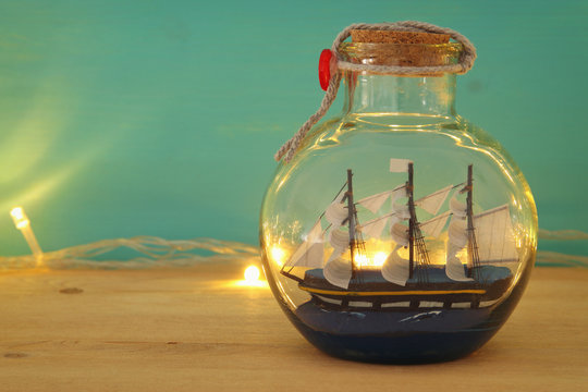 nautical concept image with sail boat in the bottle and gold garland lights over wooden table. Selective focus.
