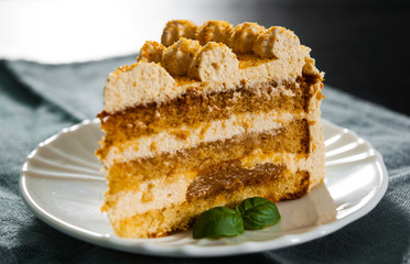 Slice of layered honey cake in a plate on wooden table