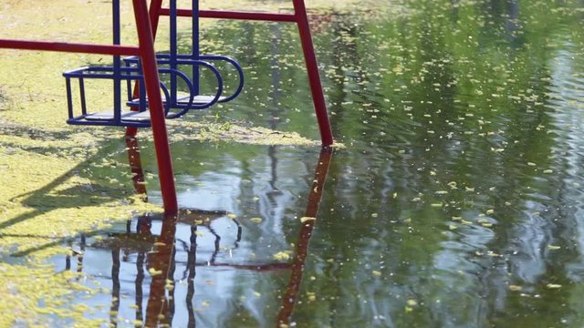 Flooded children playground with lonely empty swings on sunny spring morning.