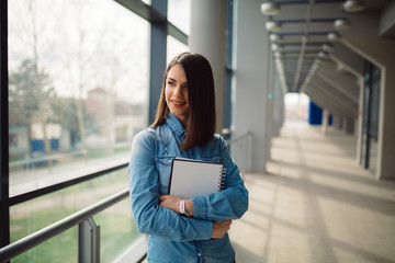 Attractive smiling student is holding notes while standing in corridor