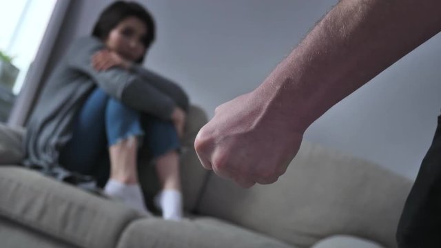 Concept of domestic violence in family, male fist afraid Asian woman sitting on the couch in the background 50 fps