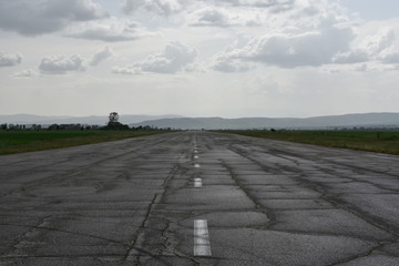 Abandoned runway used as rally racetrack. Cracks and car tire tracks seen on the wet after the spring rain asphalt surface. 