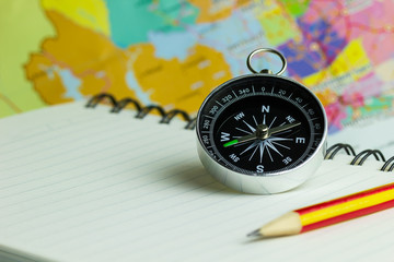 Compass notebook and pencil laid on a paper map. The concept record of travel.