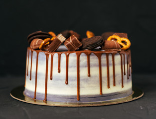 Chocolate cake with cookies and sweets, dietary on a black background. Close-up view from the front. Creamy with lint. Caramel and sugar.