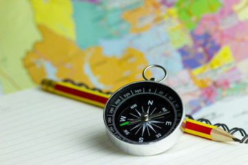 Compass notebook and pencil laid on a paper map. The concept record of travel.