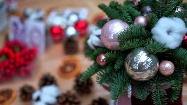 Christmas composition: pine tree branches, pink and silver christmas tree toys and cotton flower balls in gift box on plastic wrap, close-up. Craft supply for handcrafted decorations on wooden table.