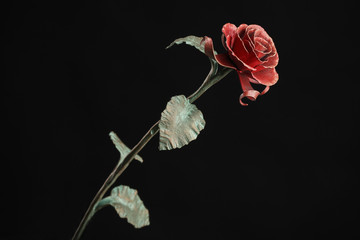 The metal rose with a red bloom and a green stalk, on black background.