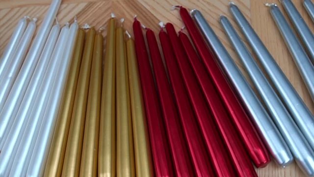 White, red, gold and silver long taper candles on light wooden surface, close-up. Supply for handcrafted table centerpiece arrangement on wooden table. Christmas holiday atmosphere.