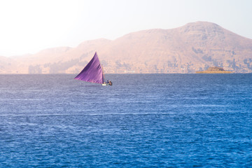 Fototapeta na wymiar Traditional small sailing boat with triangle violet sail on Titicaca Lake, Peru and Bolivia, South America.