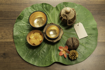 Two golden bowl with flower shape of candle on green leaf