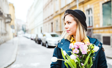 Fototapeta premium Young woman with flowers in sunny spring town.