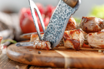 Appetizing meat cooked on an open fire that begins to cut with an original knife and fork. Cutlery for eating meat.