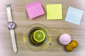 Flat lay. Beautiful ladies watch. Cup of tea with lemon. Stickers for notes, cookies and marshmallows on the table