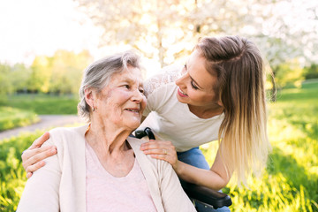 Elderly grandmother in wheelchair with granddaughter in spring nature.