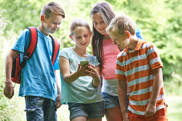 Group Of Children Geocaching Using Mobile Phone In Forest