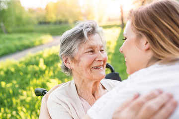 Elderly grandmother in wheelchair with granddaughter in spring nature.