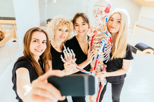 Selfie portrait of four happy smilling team female pilates instructor hugging with skeleton model in modern pilates studio interior. Sport, fitness, lifestyle, gesture and team work concept.