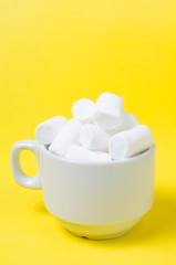 White marshmallows in a coffee mug on a bright yellow background.