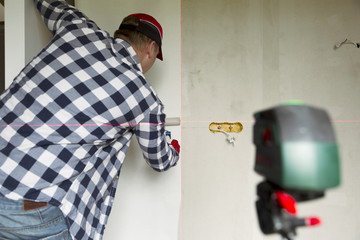 Glueing wallpapers at home. Young man, worker is putting up wallpapers on the wall. Home renovation concept