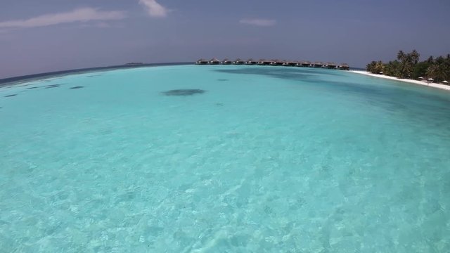 White sand beach in Vakarufalhi atoll, Maldives, Asia, Indian Ocean. People swimming and relaxing during vacation in luxury resort. Crystal clear sea water, coral reef and palms. Fisheye view