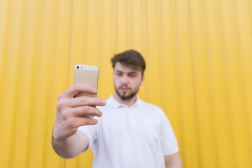 Happy man on a yellow background makes for selfie smartphone in hand. Focus on the smartphone