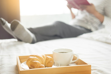 Woman reading book or newspaper and drinking coffee breakfast on bed during the morning