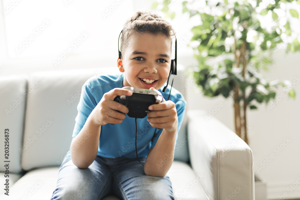 Wall mural black boy play video game on sofa with headset