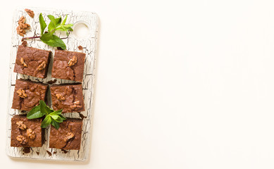 Brownie sweet chocolate dessert with walnuts and meant leaves on retro board with copy space on pastel beige background.
