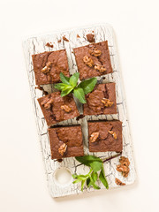 Brownie sweet chocolate dessert with walnuts and meant leaves on retro board with copy space on pastel beige background.