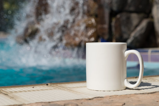 White blank coffee mug mock up, set on the poolside with a waterfall in the background.	Perfect for businesses selling mugs, just overlay your quote or design on to the image.