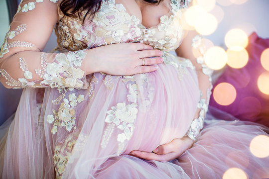 Beautiful pregnant girl in pink dress. Closeup of round tummy