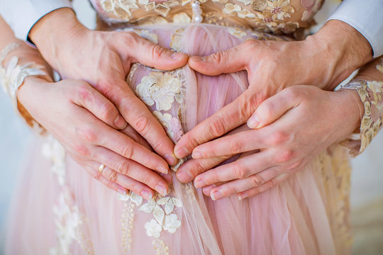 Pregnant girl in pink dress, hands on stomach in heart shape