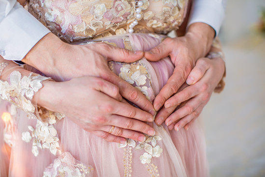 Pregnant girl in pink dress, hands on stomach in heart shape, closeup