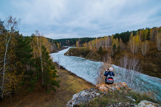 Rear elevated view of young female hiker photographing river from rocks, Kislokan, Evenk, Russia