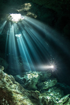 Male diver diving in underground river (cenote) with sun rays and rock formations, Tulum, Quintana Roo, Mexico