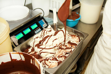 Woman working at ice cream factory is decorations of creamy vanilla ice cream with chocolate dressing in steel container. Pouring chocolate in the tray with frozen ice cream. Beautiful dessert, sweet.