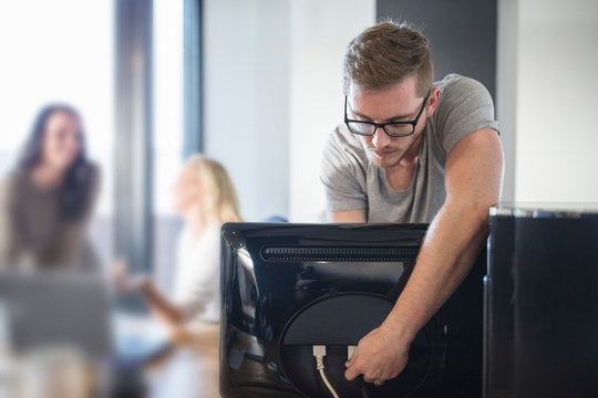 Computer technician attaching cable to computer in office