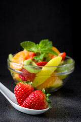 Strawberries on a spoon and assorted fruits in a bowl

