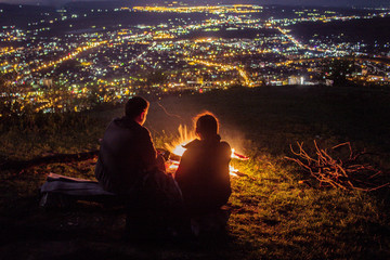A couple of girls with a guy sitting next to the fire watching the night city.