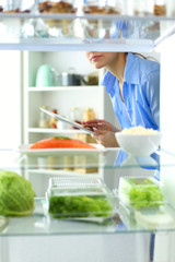 Portrait of female standing near open fridge full of healthy food, vegetables and fruits