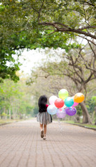 Little girl child running jumping and holding a bunch of with a colorful balloons in his hand.