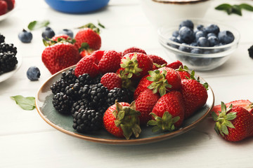 Mixed berries in glass bowls on white wooden table